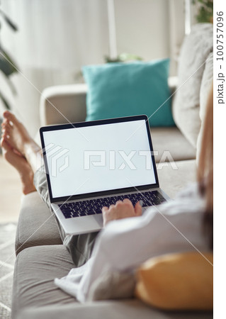 Mockup white screen laptop woman using computer lying on sofa at home, back view, focus on screen Mockup white screen laptop woman using computer lying on sofa at home, back view, focus on screen 100757096
