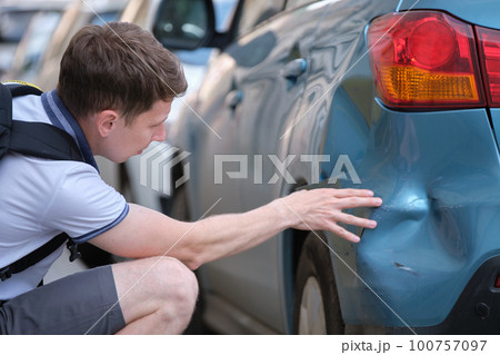 Sad male driver sitting on street side shocked looking at his dented car parked at street side. Road safety and vehicle insurance concept Sad male driver sitting on street side shocked looking at his dented car parked at street side. Road safety and vehicle insurance concept 100757097
