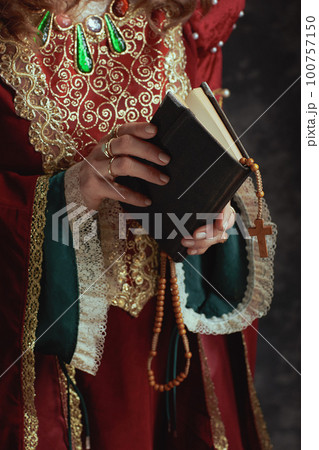 Closeup on medieval queen in red dress with book and rosary 100757150