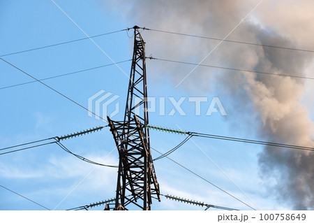 High voltage electric pylons against coal power plant high pipes with black smoke moving upwards polluting atmosphere. Production of electrical energy with fossil fuel concept 100758649