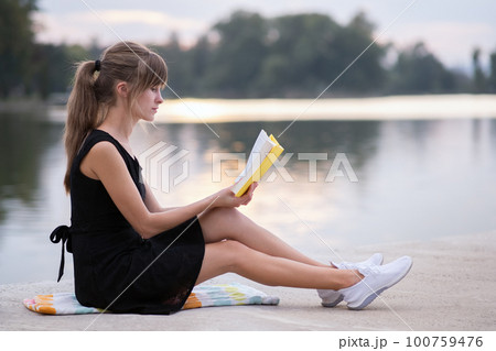 Female student sitting in summer park reading textbook outdoors. Education and sudy concept. Female student sitting in summer park reading textbook outdoors. Education and sudy concept. 100759476