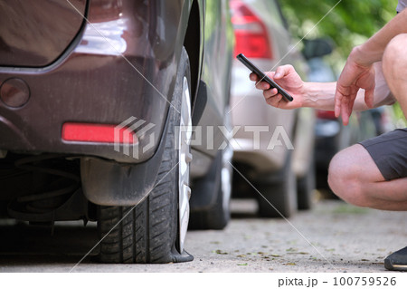 Driver calling road service for assistance having vehicle trouble with punctured flat tire on car parked on roadside Driver calling road service for assistance having vehicle trouble with punctured flat tire on car parked on roadside 100759526