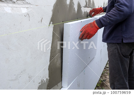Construction worker installing styrofoam insulation sheets on house facade wall for thermal protection. 100759659
