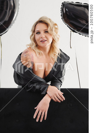 a naked blonde with tattoos in a black coat by a black sofa. birthday 100760500