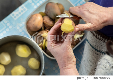 Closeup of woman hands peeling potatoes with a kitchen knife. Closeup of woman hands peeling potatoes with a kitchen knife. 100760655