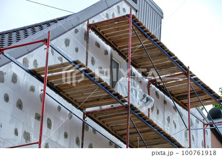Building facade under renovation works with construction scaffolding frame. Wall insulation with styrofoam sheets for energy efficient home 100761918