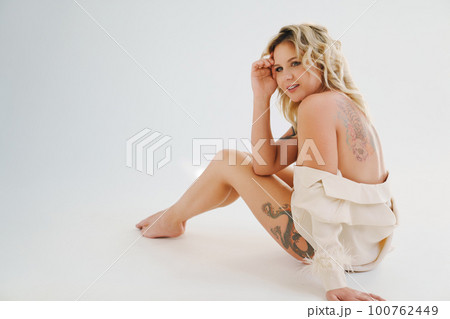a gentle naked blonde woman in a white shirt on the floor.  100762449