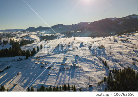 Aerial view of small village with scattered houses on snow covered hills in winter and bare dark Carpathian mountains in Ukraine. Aerial view of small village with scattered houses on snow covered hills in winter and bare dark Carpathian mountains in Ukraine. 100762650
