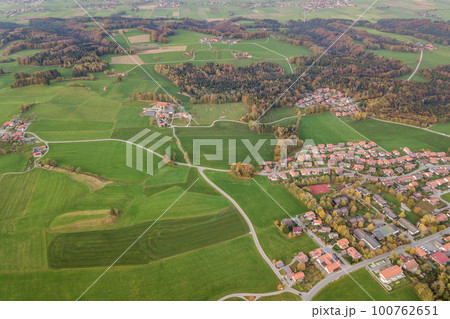Aerial view of small town with red tiled roofs among green farm fields and distant forest in summer. 100762651