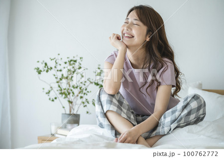 ベッドに座った笑顔の若い女性　 100762772