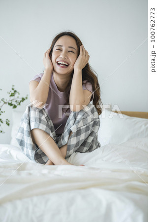 ベッドに座った笑顔の若い女性　 100762773