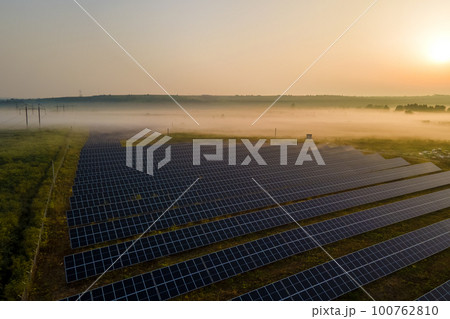 Aerial view of large sustainable electrical power plant with rows of solar photovoltaic panels for producing clean electric energy in evening. Concept of renewable electricity with zero emission Aerial view of large sustainable electrical power plant with rows of solar photovoltaic panels for producing clean electric energy in evening. Concept of renewable electricity with zero emission 100762810