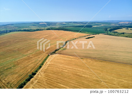 Aerial landscape view of yellow cultivated agricultural field with dry straw of cut down wheat after harvesting 100763212