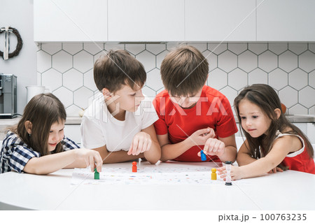 Four blissful, smiling kids playing board games and choosing colorful figures on table in kitchen. Children development Four blissful, smiling kids playing board games and choosing colorful figures on table in kitchen. Children development 100763235
