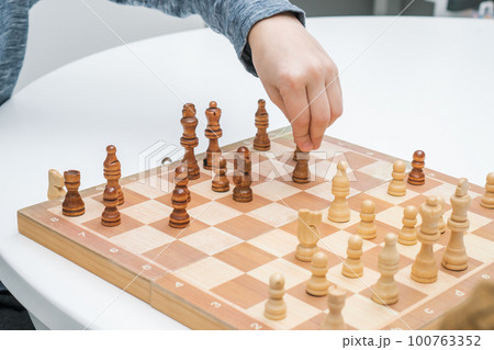 Unrecognizable cropped boy hand hold and move chess pawn, play chess on wooden board on white table. Sport board game Unrecognizable cropped boy hand hold and move chess pawn, play chess on wooden board on white table. Sport board game 100763352
