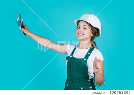 confident kid use spatula while repairing. concept of building and renovation. happy girl use spatula tool. teen builder wear safety helmet. young worker in protective hard hat confident kid use spatula while repairing. concept of building and renovation. happy girl use spatula tool. teen builder wear safety helmet. young worker in protective hard hat 100765603