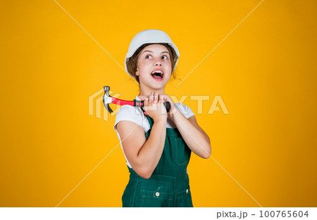 Examining your car. kid wear helmet on construction site. teen girl builder with building tool hammer. child on repairing work. concept of renovation in workshop. busy professional carpenter 100765604