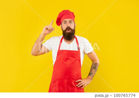 Surprised man in toque and apron got idea keeping finger raised yellow background, cook 100765774