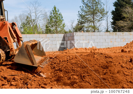 An excavator scoop is moved and levelling as it moves along land at construction site 100767248