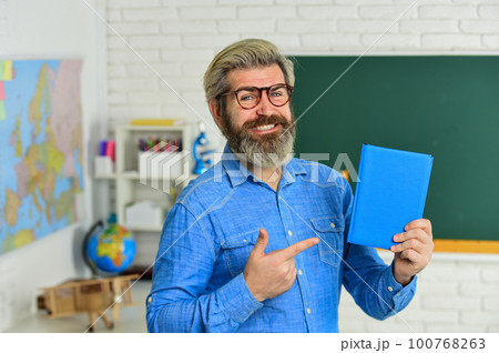 try this one. literature and language learning. strict teacher in glasses. teacher check knowledge. are you ready for exam test. man tutor in classroom. use notebook or book. back to school 100768263