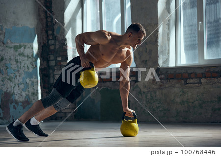 Hands exercises. Young handsome man with muscular, strong, fit body training indoors, lifting weights standing in plank. Concept of sportive lifestyle 100768446