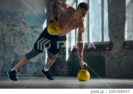 Young handsome man with muscular, strong, fit body training indoors with sports equipment on a daytime. Lifting weights. Concept of sportive lifestyle 100768447