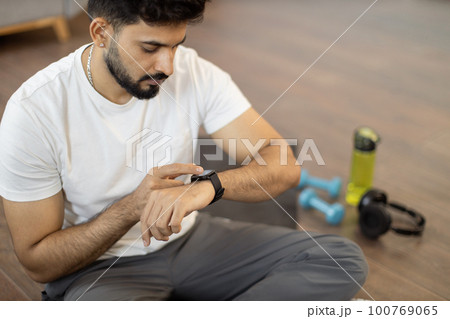 Arabic man setting heart-rate watch during home training 100769065