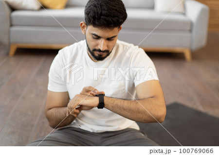 Arabic man setting heart-rate watch during home training 100769066