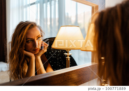 A pretty Caucasian woman looks at her reflection in the mirror with boredom. The concept of self-isolation, psychology and introvertism A pretty Caucasian woman looks at her reflection in the mirror with boredom. The concept of self-isolation, psychology and introvertism 100771889