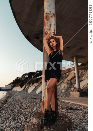 Fashion. Sexy blonde Woman in black mini dress posing at a pillar. In the background, the embankment and the mountain Fashion. Sexy blonde Woman in black mini dress posing at a pillar. In the background, the embankment and the mountain 100771891