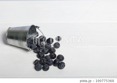 Overturned decorative bucket. Scattered large blueberries. International day without diets. On a white background. Close-up. Overturned decorative bucket. Scattered large blueberries. International day without diets. On a white background. Close-up. 100775368