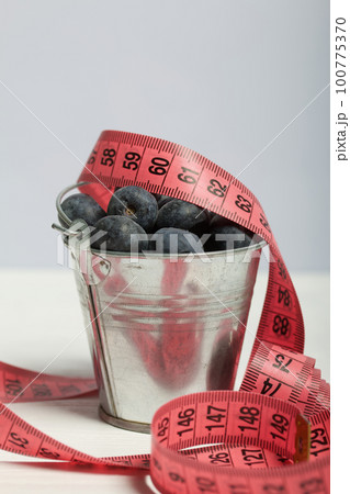 Large blueberries in a decorative bucket. Measuring tape for measuring the waist. International day without diets. On a white background. Close-up. 100775370