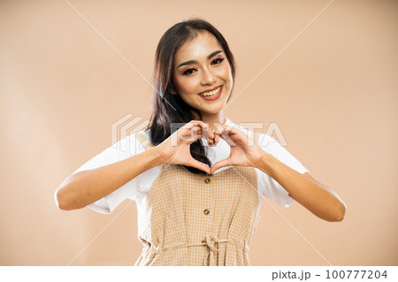 smiling asian woman in casual clothes standing with love hand gesture smiling asian woman in casual clothes standing with love hand gesture 100777204
