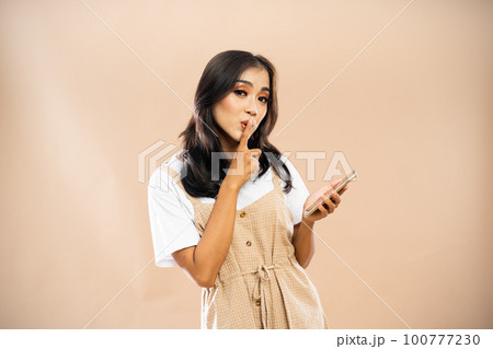 asian woman closing her mouth using her finger while holding the phone 100777230