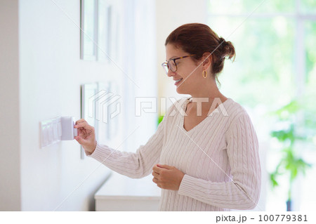 Woman adjusting thermostat. Central heating. 100779381
