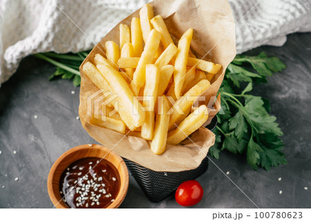 Large serving of French fries stand in craft paper with barbecue sauce, sesame seeds, cherry tomatoes and green parsley 100780623