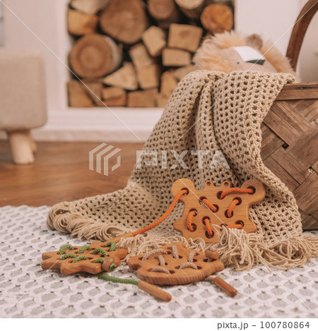 Children's wooden toy with holes for lacing with orange cord on beige blanket on background of fireplace. Square frame 100780864