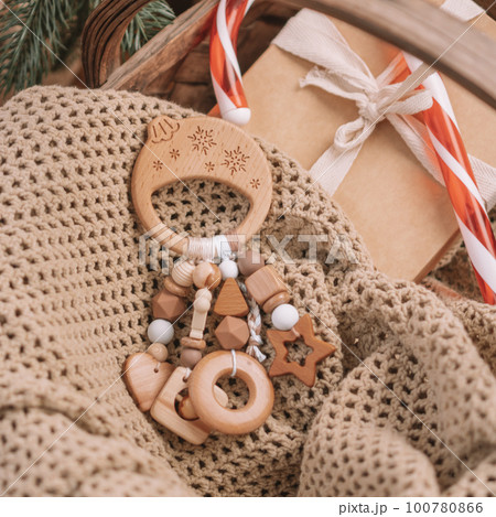 Wooden Christmas ball-shaped childrens teether with silicone beads lies among gifts on blanket under Christmas tree 100780866