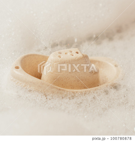 Cute beige small silicone toy boat with holes on top floating in bubble bath. Baby toys, toys for developing creativity. 100780878