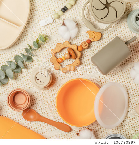 Pastel silicone kit of tableware, cutlery, accessories and wooden toys for children on white cotton cloth background. 100780897