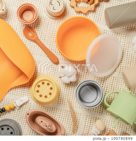 Pastel silicone set of tableware, cutlery, bib, accessories and wooden toys for children on white cloth background. 100780899