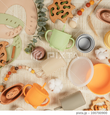 Pastel silicone kit of tableware, cutlery, bibs, accessories and wooden toys for children on white cloth background. Pastel silicone kit of tableware, cutlery, bibs, accessories and wooden toys for children on white cloth background. 100780900