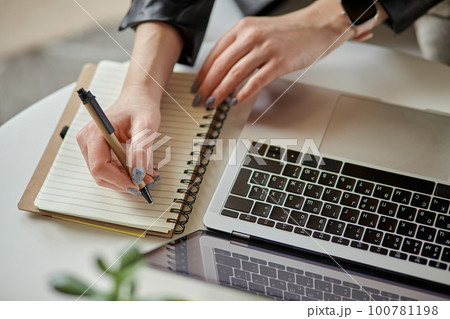 Close up woman hand using laptop and making notes in notebook sitting at workplace at home, remote work Close up woman hand using laptop and making notes in notebook sitting at workplace at home, remote work 100781198