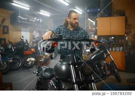 Mature male biker on his new motorbike in garage 100783200