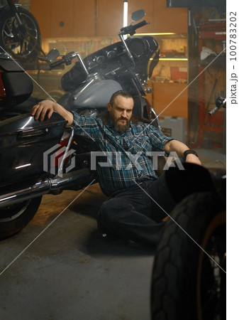 Serious biker sitting on floor and thinking searching way to repair motorcycle 100783202