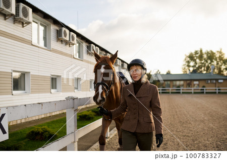 Attractive smiling woman equestrian walking horse in outdoor paddock Attractive smiling woman equestrian walking horse in outdoor paddock 100783327