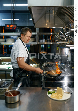 Chef throwing on air hot pasta in frying pan, cooking process 100783370