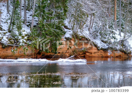 Red sandstones on the bank of the river Salaca. Red sandstone rock in Bezdeligu winter. Skanaiskalns nature park Red sandstones on the bank of the river Salaca. Red sandstone rock in Bezdeligu winter. Skanaiskalns nature park 100783399
