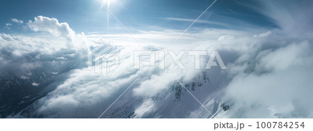 Alpine landscape with peaks covered by snow and clouds. Magical clouds covering peaks of the mountains at the famous St. Anton am Arlberg ski resort. 100784254