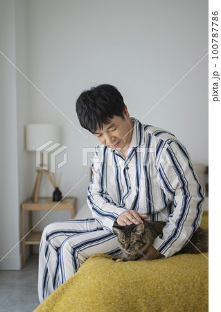 ベッドに座って猫を撫でるパジャマ姿の50代男性 ベッドに座って猫を撫でるパジャマ姿の50代男性 100787786